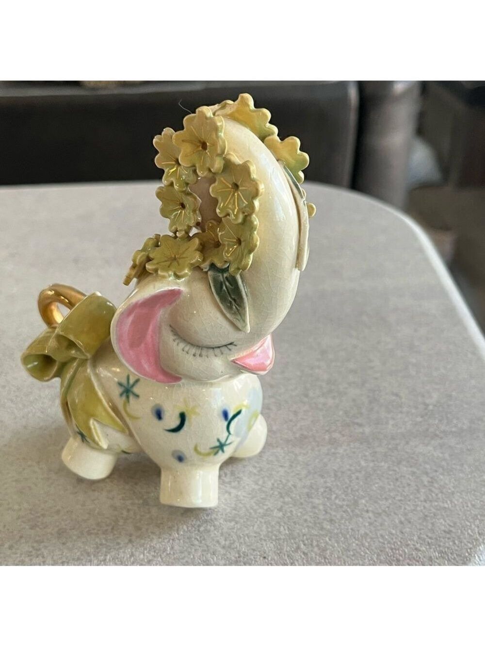 A decorated Elephant? Ceramic. Pink ears. Nose in air. Flowers on trunk. Eyelash